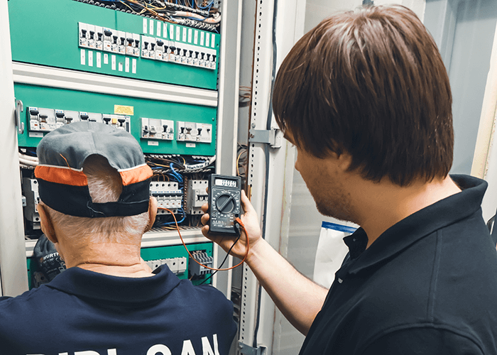 pracownicy obsługi technicznej przy instalacji elektrycznej z multimetrem
